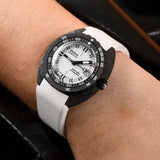 A close-up of a wrist wearing a DOXA SUB 300 CARBON Chronometer 42.50mm Watch 822.70.011.23 with a black carbon fiber bezel, white dial, and white strap, shown against a dark leather background.