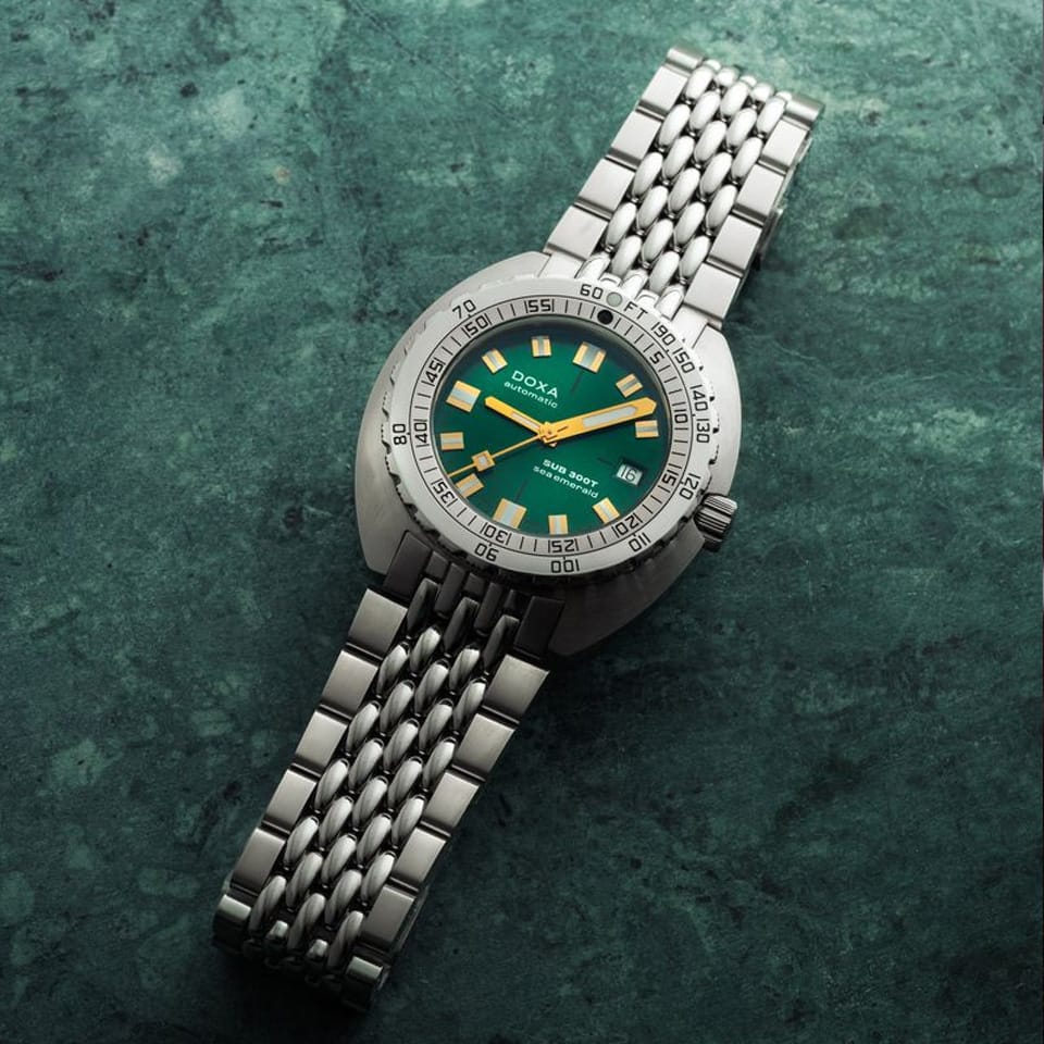 DOXA SUB 300T Sea Emerald Automatic 42.50mm Watch 840.10.131.10 with a green dial and matching green bezel, resting diagonally on a textured dark green surface.