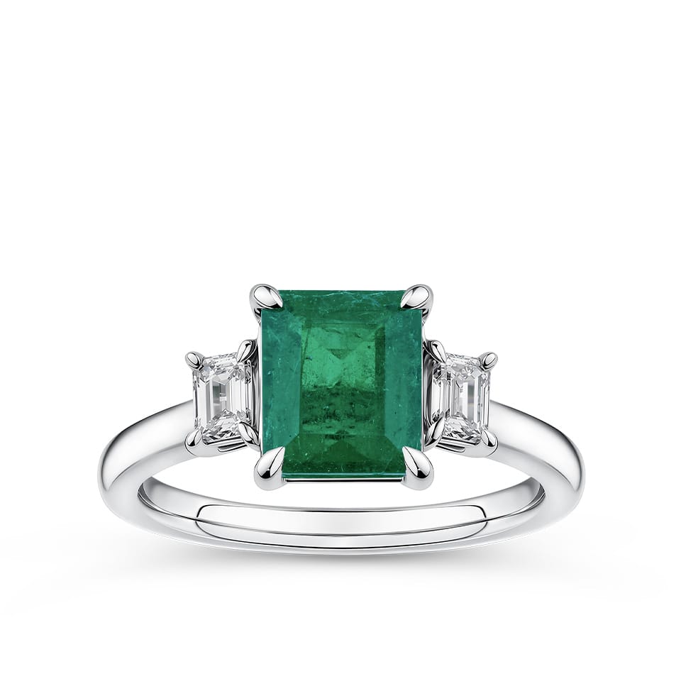1.62 Carat Emerald and 0.40 Carat TW Diamond Trilogy Ring in 18ct White Gold — A 1.62 carat emerald-cut emerald sits at the centre of this trilogy design, flanked by two natural emerald-cut diamonds of H-I colour and VS-SI clarity. The 18ct white gold setting provides a polished, cool contrast to the emerald's rich green hue.