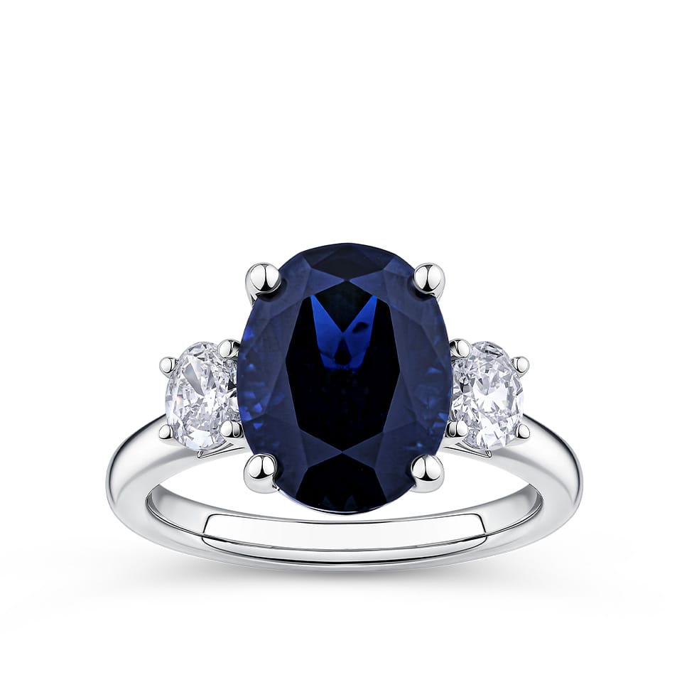 5.54 Carat Sapphire and 0.40 Carat TW Diamond Trilogy Ring in 18ct White Gold — A 5.54 carat oval-cut blue sapphire sits at the centre of this trilogy design, flanked by two natural oval-cut diamonds of G-H colour and VS-SI clarity. The 18ct white gold setting provides a polished, cool contrast to the sapphire's deep blue hue.