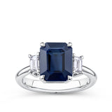 3.68 Carat Sapphire and 0.42 Carat TW Diamond Trilogy Ring in 18ct White Gold — A 3.68 carat emerald-cut blue sapphire sits at the centre of this claw-set trilogy design, flanked by two natural emerald-cut diamonds of G colour and VS clarity. The 18ct white gold setting provides a polished, cool contrast to the sapphire's deep blue hue.