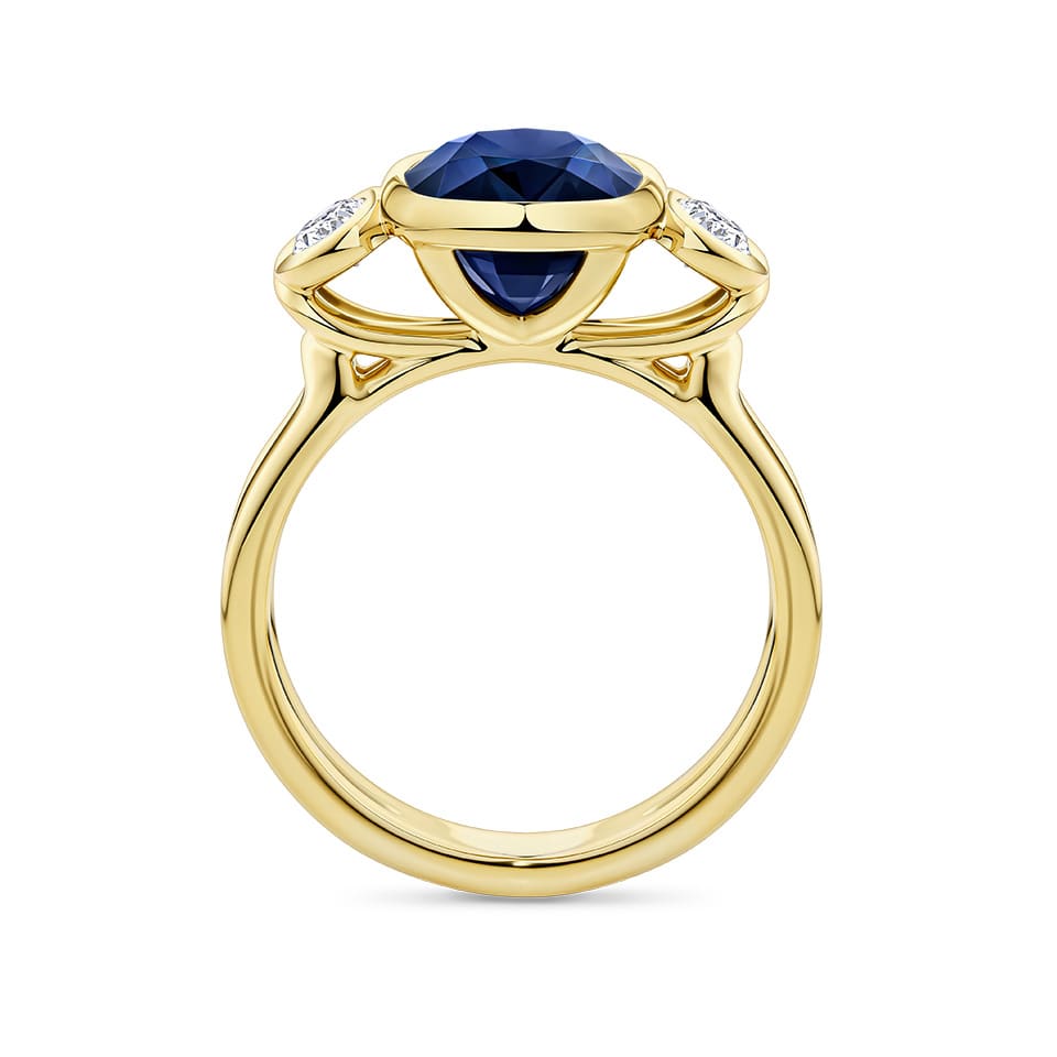 Angled view of the Sapphire and Diamond Trilogy Ring in 18ct yellow gold by Hardy Brothers, highlighting the bezel-set sapphire and diamond side stones.