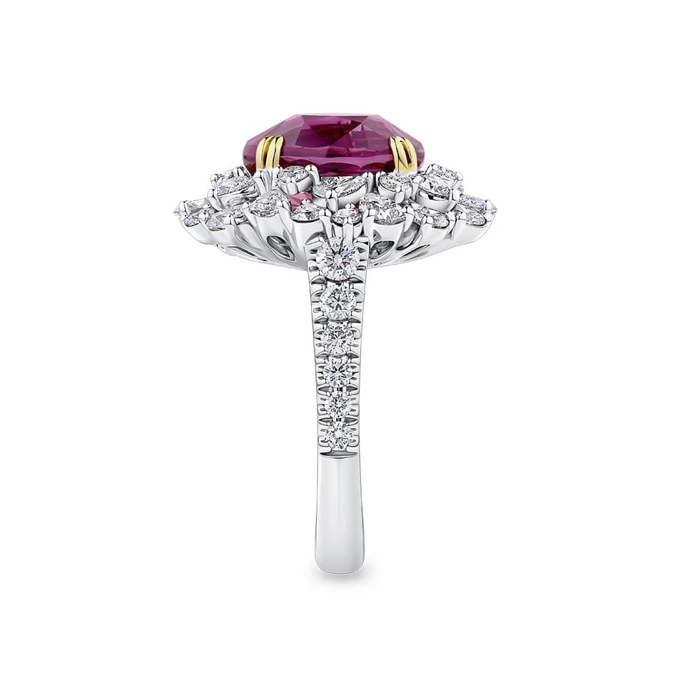 VAULT® 6.09 Carat TW Oval Cut Mozambique Ruby and 2.44 Carat TW Diamond Halo Ring in 18ct Yellow and White Gold — A side profile shows the diamond-set shank rising to meet the elevated ruby and halo setting. The two-tone gold construction is visible where the yellow gold claws meet the white gold mount.