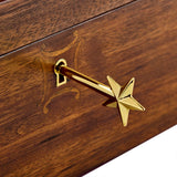 A close-up of a polished gold star-shaped drawer pull handle mounted on a dark brown wooden drawer front with an engraved decorative motif.