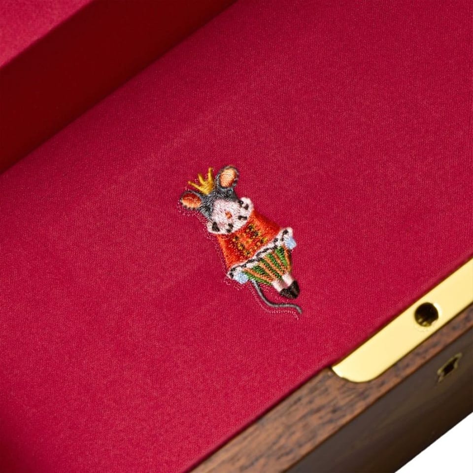 Embroidered mouse design on a red fabric surface with a gold and wooden border.