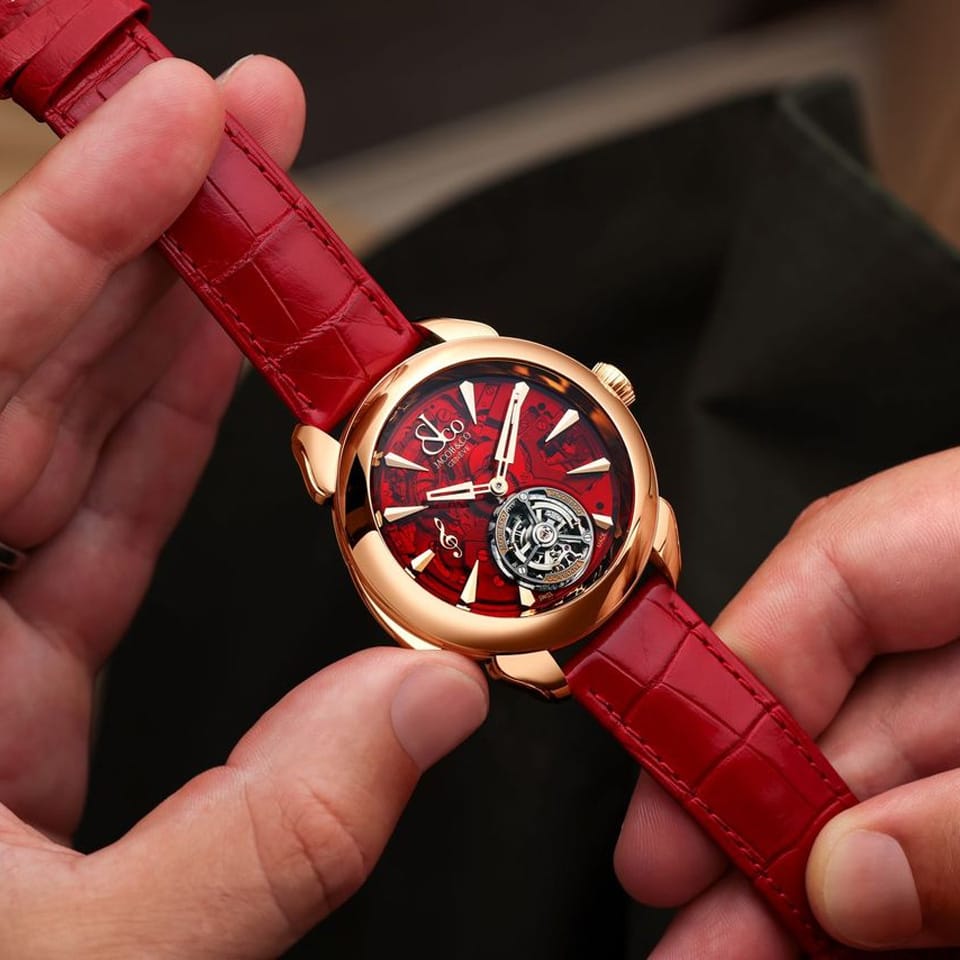 Close up view of the Jacob & Co. Palatial Flying Tourbillon Minute Repeater 18K Rose Gold Manual 43mm Watch, reference PT500.40.NS.AC.A, detailing the applied brushed 18K Rose Gold G Clef and hour markers on the red mineral crystal dial. The skeletonized metronome hands and open tourbillon are visible in fine detail.