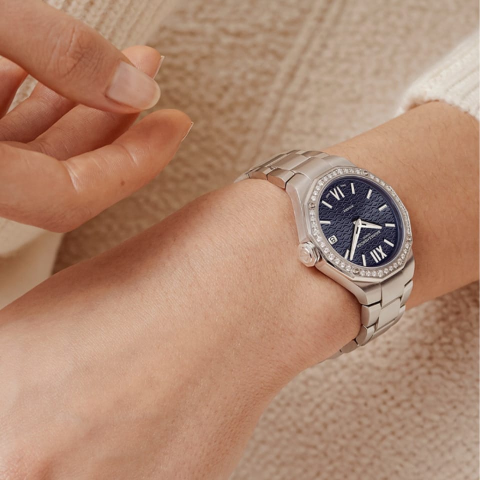 The Baume & Mercier Riviera M0A10765 worn on a woman's wrist in a lifestyle setting, showcasing the 33mm twelve-sided stainless steel case with its diamond-set bezel catching the light against the skin, the deep night blue dial visible beneath the sapphire crystal, and the integrated steel bracelet sitting elegantly on the wrist.