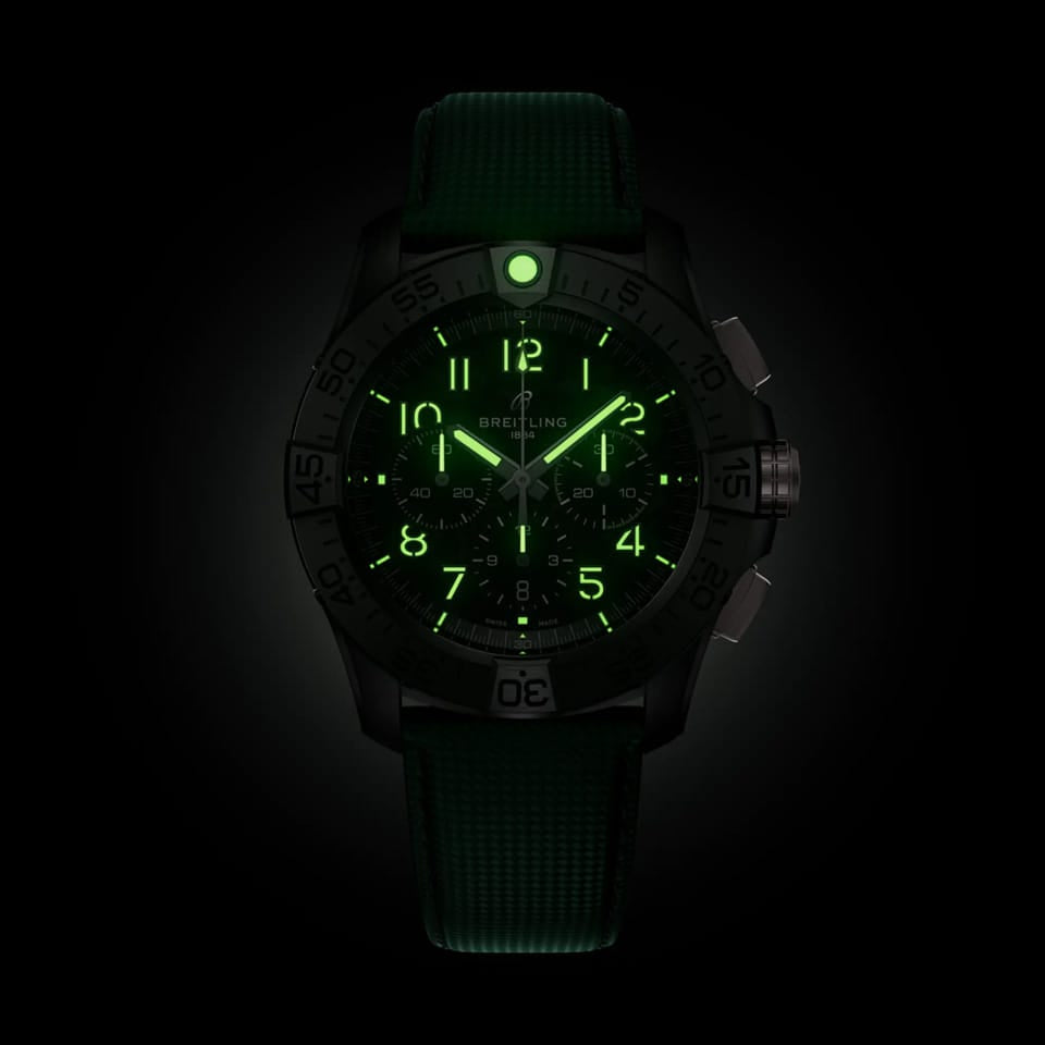 Breitling Super Avenger B01 Chronograph 46mm Watch SB0148101B1X1 shows the luminous properties of its dial markers and hands in low light. The military-inspired carbon dial remains legible against the illuminated ceramic case in dark conditions.