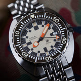 Close-up of a DOXA ARMY Automatic 42.50mm Watch 785.10.031.10with a black rotating bezel, cream dial, orange hour markers, and a matching metal link bracelet.