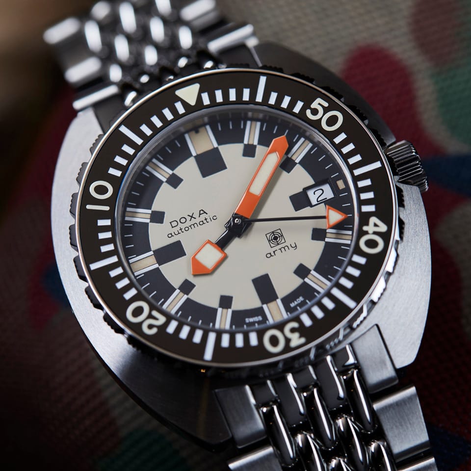 Close-up of a DOXA ARMY Automatic 42.50mm Watch 785.10.031.10with a black rotating bezel, cream dial, orange hour markers, and a matching metal link bracelet.