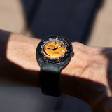 A close-up of a wrist wearing a DOXA SUB 300 Carbon Chronometer 42.50mm Watch 822.70.351.20 with a black strap, black bezel, and a vibrant orange dial.