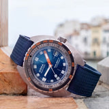 Front view of DOXA SUB 300 Ti5 Caribbean watch, 42.5mm grade 5 titanium cushion case, Caribbean Blue dial with oversized orange minute hand, patented dual-scale dive bezel, screw-down crown, and blue rubber strap with folding clasp — Ref. 823.50.201.32