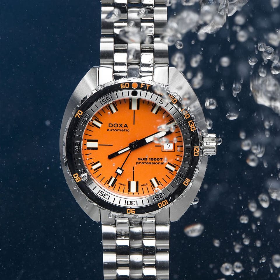 A DOXA SUB 1500T Professional Automatic 45mm Watch 883.10.351.10automatic watch with a vibrant orange dial and a silver stainless steel link bracelet, shown against a dark blue background with water droplets and bubbles.