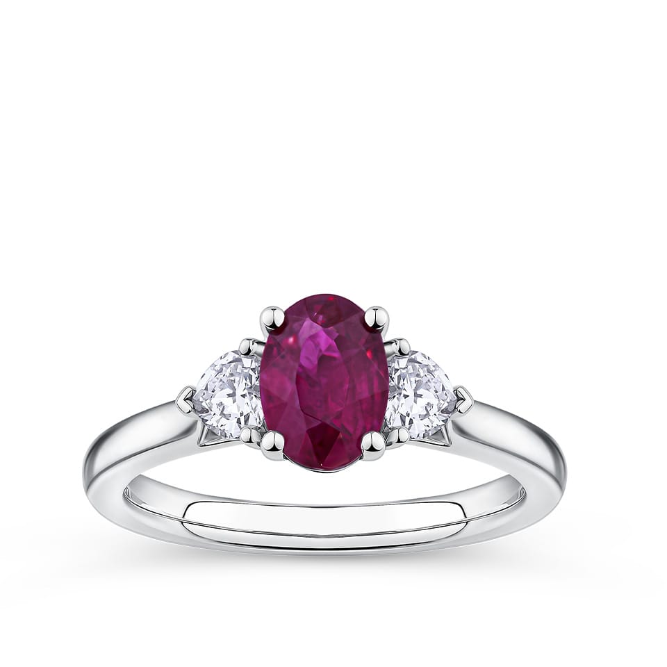 1.39 Carat Burmese Ruby and 0.36 Carat TW Diamond Trilogy Ring in 18ct White Gold — A certified oval-cut Burmese ruby sits at the centre of this trilogy design, flanked by two heart-cut diamonds with their points facing along the band. The 18ct white gold setting provides a polished, cool contrast to the ruby's deep red hue.