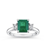 1.62 Carat Emerald and 0.40 Carat TW Diamond Trilogy Ring in 18ct White Gold — A 1.62 carat emerald-cut emerald sits at the centre of this trilogy design, flanked by two natural emerald-cut diamonds of H-I colour and VS-SI clarity. The 18ct white gold setting provides a polished, cool contrast to the emerald's rich green hue.