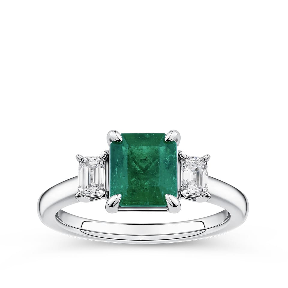 1.81 Carat Emerald and 0.30 Carat TW Diamond Trilogy Ring in 18ct White Gold — A 1.81 carat emerald-cut emerald sits at the centre of this trilogy design, flanked by two natural emerald-cut diamonds of H-I colour and VS-SI clarity. The 18ct white gold setting provides a polished, cool contrast to the emerald's rich green hue.