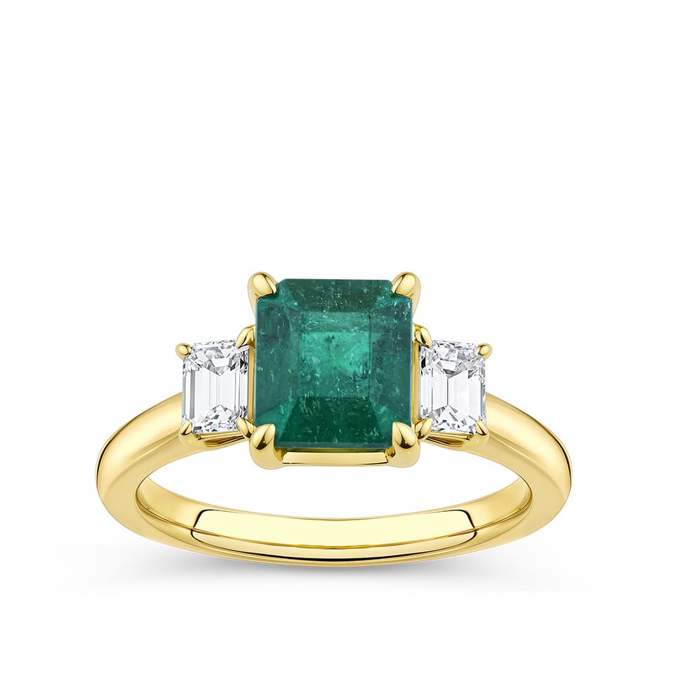 2.10 Carat Emerald and 0.40 Carat TW Diamond Trilogy Ring in 18ct Yellow Gold — A 2.10 carat emerald-cut natural emerald sits at the centre of this trilogy design, flanked by two natural emerald-cut diamonds. The 18ct yellow gold setting provides a warm, rich contrast to the emerald's vivid green hue.
