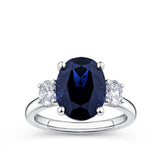 5.54 Carat Sapphire and 0.40 Carat TW Diamond Trilogy Ring in 18ct White Gold — A 5.54 carat oval-cut blue sapphire sits at the centre of this trilogy design, flanked by two natural oval-cut diamonds of G-H colour and VS-SI clarity. The 18ct white gold setting provides a polished, cool contrast to the sapphire's deep blue hue.