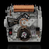 A highly detailed, vintage-inspired mechanical music box or model machine with exposed silver-toned metal gears, a large copper cylinder, black decorative plates, and gold lettering that reads 'GODEATHER WALTZ LOVE THEME' and 'JACob & CO'.