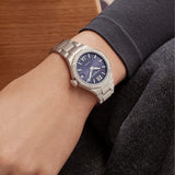 Close-up wrist shot of the Baume & Mercier Riviera M0A10765, emphasising the brilliance of the 44 diamond-set bezel sparkling against the polished twelve-sided case, the rich night blue dial with its wave pattern transfers, and the elegant integrated stainless steel bracelet completing the look.