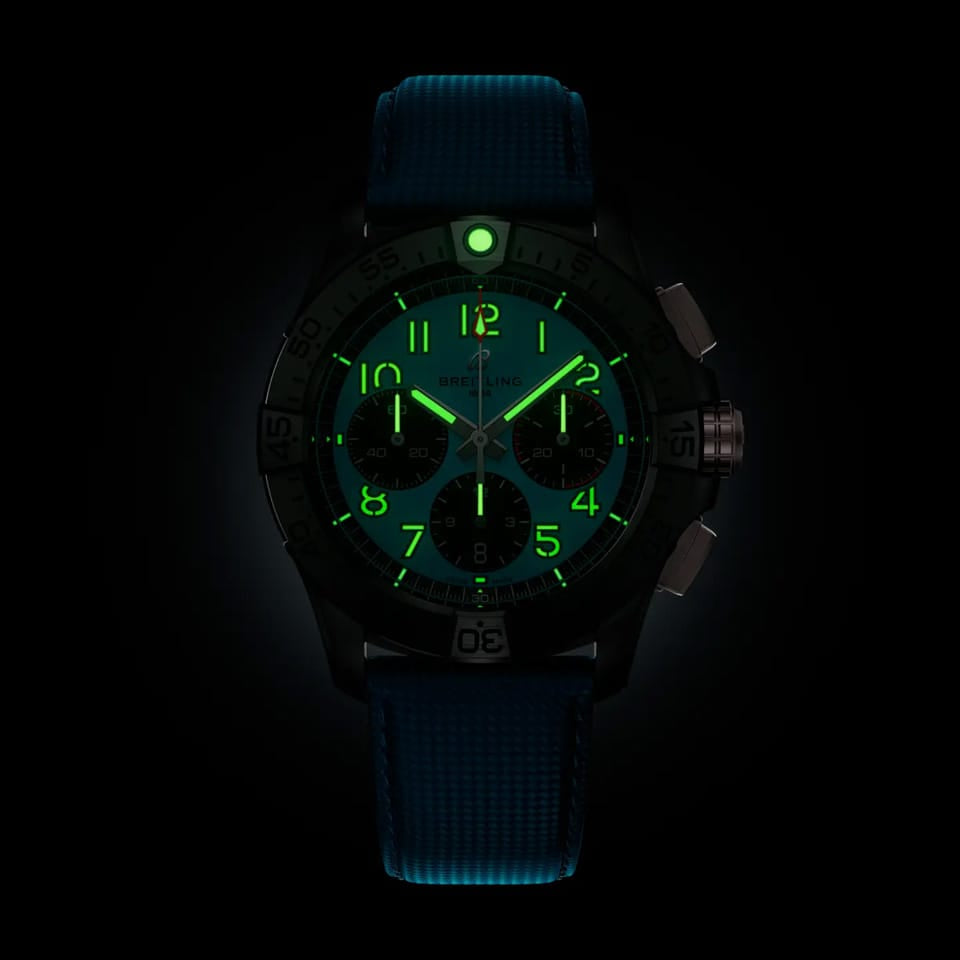 Breitling Avenger B01 Chronograph 42mm Watch SB0146101L1X1 shows the luminous properties of its dial markers and hands in low light. The military-inspired turquoise dial remains legible against the illuminated ceramic case in dark conditions.