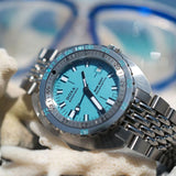 A DOXA SUB 300T Aquamarine Automatic 42.50mm Watch 840.10.241.10 with a bright turquoise dial and matching turquoise bezel markings, styled on white coral with a blurred blue-and-white diving mask in the background.
