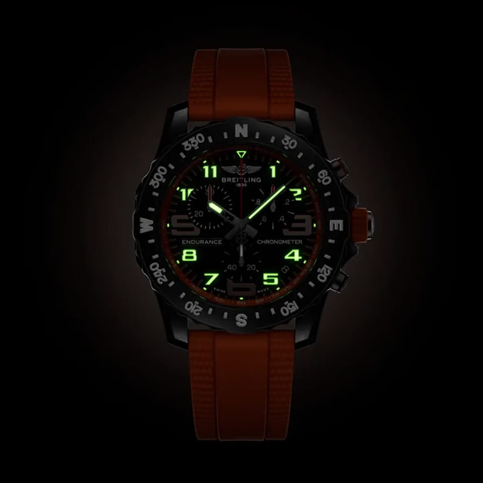 Breitling Endurance Pro Quartz Chronograph 44mm Watch X82310A51B1S2 shows the luminous properties of its dial markers and hands in low light. The black dial and orange accents remain legible against the illuminated Breitlight® case in dark conditions.