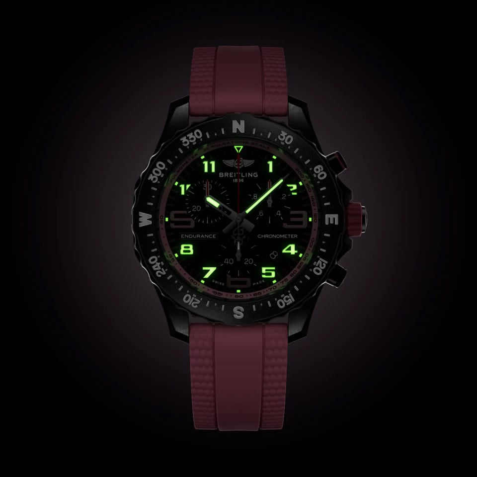 Breitling Endurance Pro Quartz Chronograph 38mm Watch X83310D41B1S1 shows the luminous properties of its dial markers and hands in low light. The black dial and pink accents remain legible against the illuminated Breitlight® case in dark conditions.