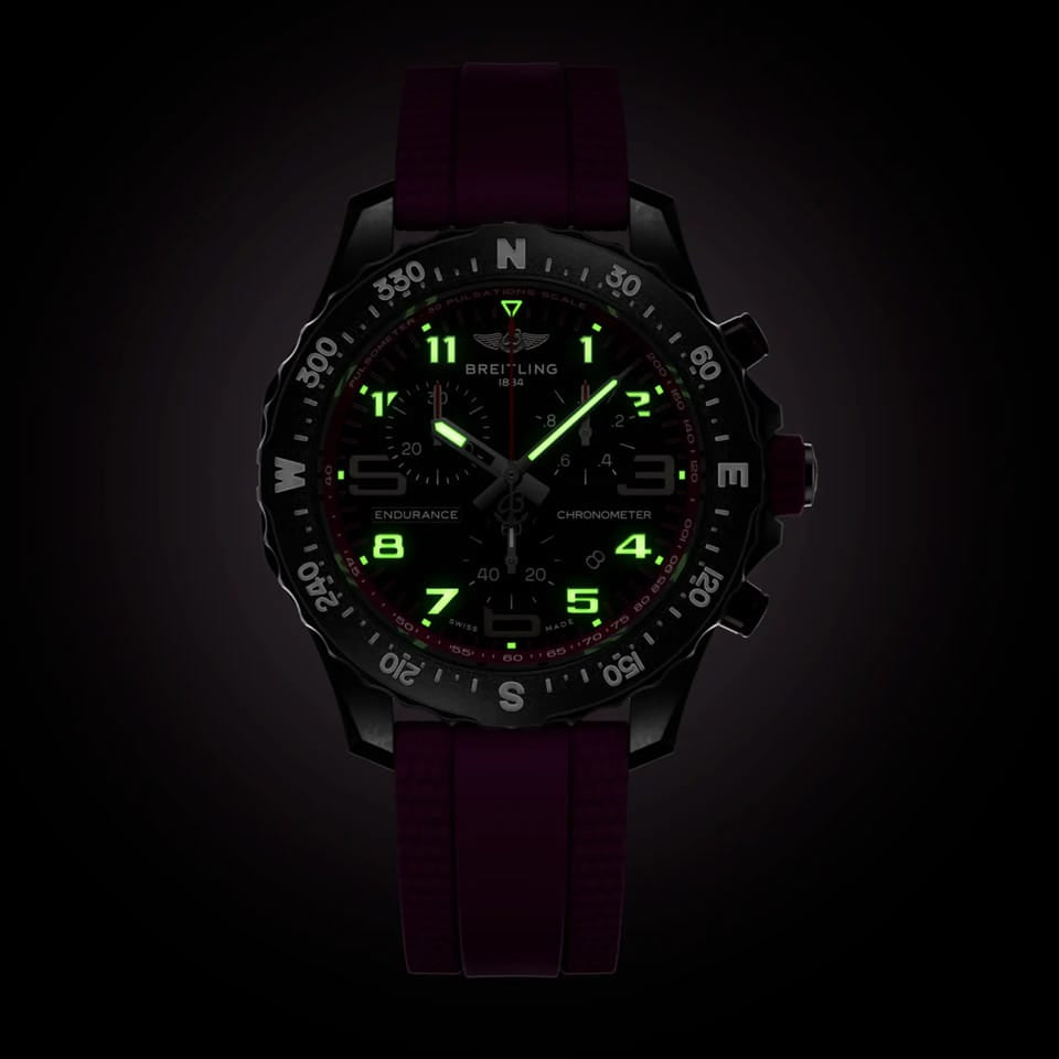 Breitling Endurance Pro Quartz Chronograph 38mm Watch X83310F61B1S1 shows the luminous properties of its dial markers and hands in low light. The black dial and purple accents remain legible against the illuminated Breitlight® case in dark conditions.