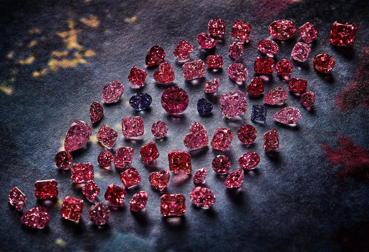 A collection of loose pink gemstones in various shapes and sizes, arranged in a curved cluster on a dark textured background.