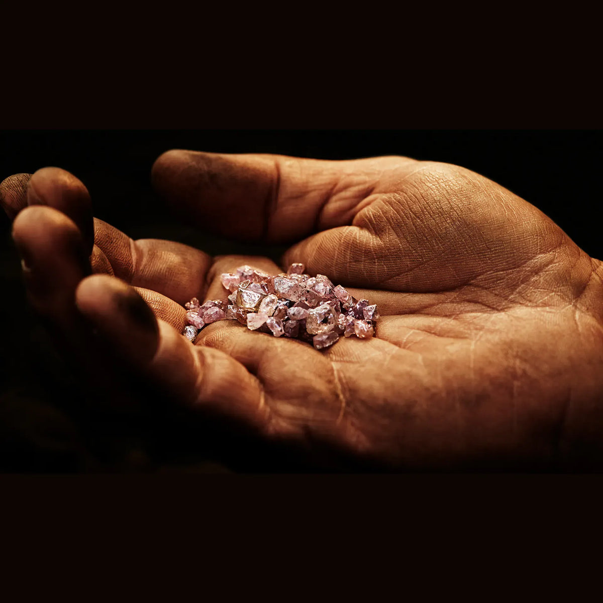 A close-up of a person's open palm holding a small pile of rough, faceted pink gemstones against a dark background.